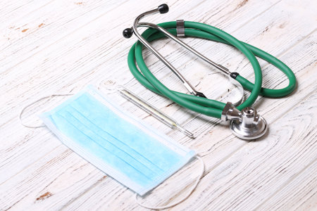 Top view of stethoscope, protective mask and mercury thermometer on white wooden background. Medical instruments concept.の写真素材