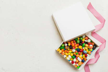 Set of different sweet candy in a paper box with a satin ribbon on a colored background. Holiday...