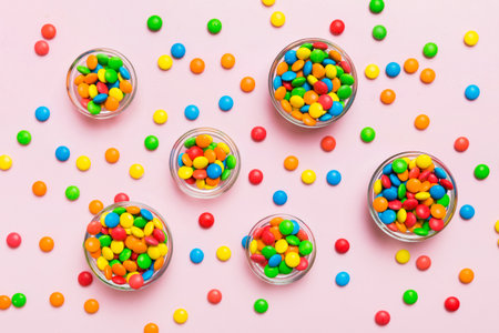 different colored round candy in bowl and jars. Top view of large variety of sweets and candies with...