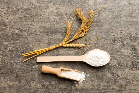 Flat lay of Wheat flour in wooden bowl with wheat spikelets on colored background.