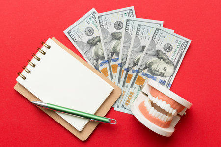 Flat lay composition with educational dental typodont model and money with notebook on colored...