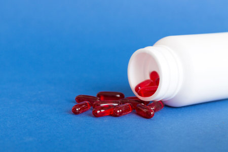 Red pills spilled around a pill bottle. Medicines and prescription pills flat lay background. Red...