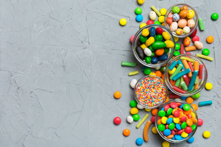different colored round candy in bowl and jars. Top view of large variety of sweets and candies with...
