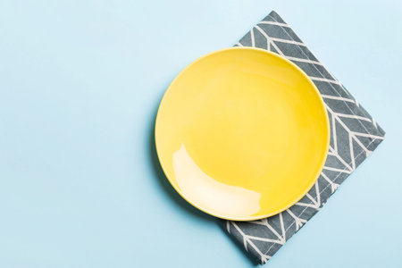 Top view on colored background empty round yellow plate on tablecloth for food. Empty dish on napkin with space for your design.