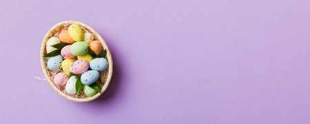 Colorful Easter eggs in wicker basket against colored background, closeup. top view with copy space.