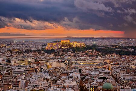 Illuminated Acropolis of Athens Greece at cloudy sky sunset with the sea and mountains at the backgroundの写真素材