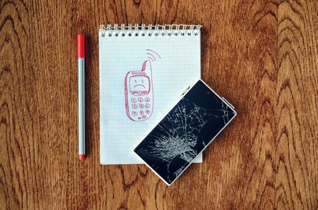 Freehand drawing of old phone in notebook. Smartphone with broken screen on wooden table. Dream, visualization desire, need a new phone conceptの写真素材