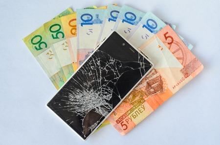 Broken smartphone lying on money banknotes on a White background. Losing money conceptの写真素材