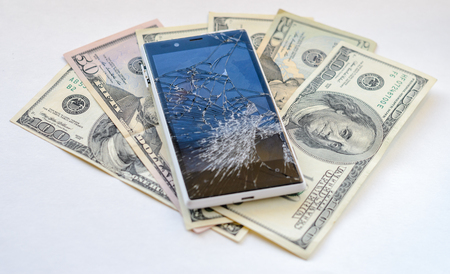Smartphone with broken display lying on money banknotes on white background. Need new smartphone conceptの写真素材