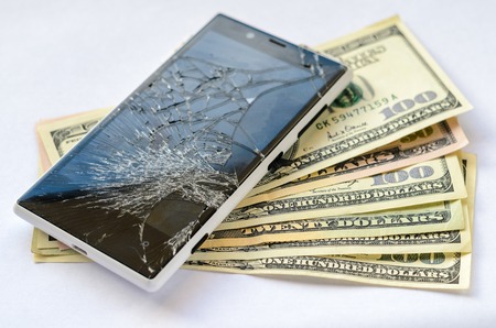 Smartphone with broken display lying on money banknotes on white background. Need new smartphone conceptの写真素材