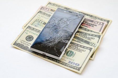 Smartphone with broken display lying on money banknotes on white background. Need new smartphone conceptの写真素材