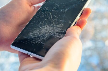White Smartphone with broken screen in human hands on blured nature backgroundの写真素材