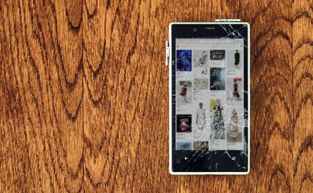 White Smartphone with broken screen on wooden table. Loss of connection concept