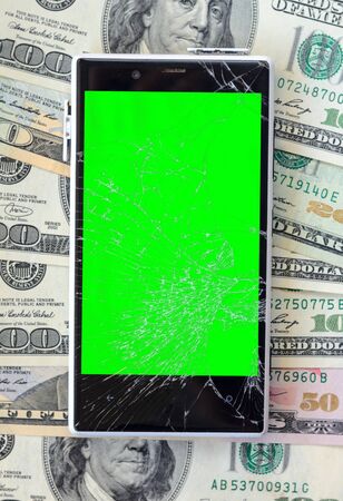 White Broken Smartphone on money banknotes background. Green chroma key display of damaged cellphone. Need new smartphone conceptの写真素材