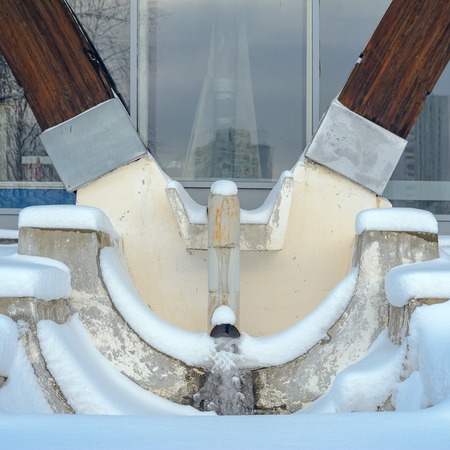 Detail of a modern wooden architecture in glued laminated timber with iced Rainwater system. V-shaped column- Element of building drain system in winter snowの写真素材
