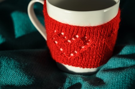Still life of Cozy Mug in red knitted mitten with heart pattern on mint color backgroundの写真素材