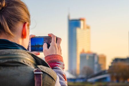 Young woman takes pictures of the city's panorama on a smartphone. City travel conceptの写真素材