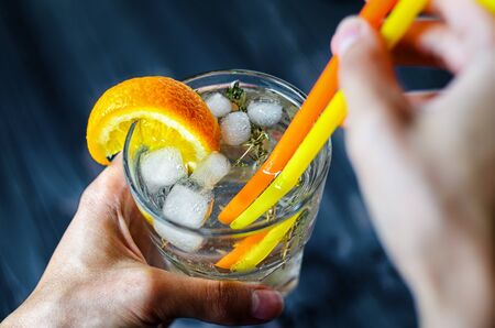 Gin tonic with ice, decorated with an orange slice and rosemary. First-person view of a soft drink in a glass cup with a pair of strawsの写真素材