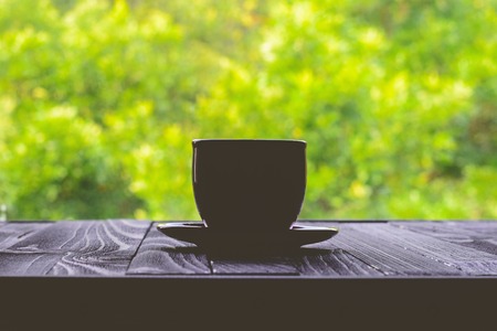 Silhouette of classical mug for espresso on a black table in a cafe on a background of green foliageの写真素材