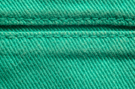 Green Denim Tissue Structure Textile Texture Close-up. Macro shot of the finishing seam on a green jeans product.の写真素材