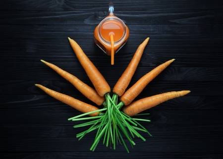 Fresh carrot juice in a glass jar with handle on a black wooden table. Carrot smoothie in a glass mug with orange straw top viewの写真素材