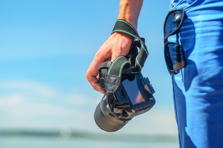Dslr camera in the hand of a man standing on coast and looking for the story. Dslr camera in a man's hand close-up against a sea horizonの写真素材