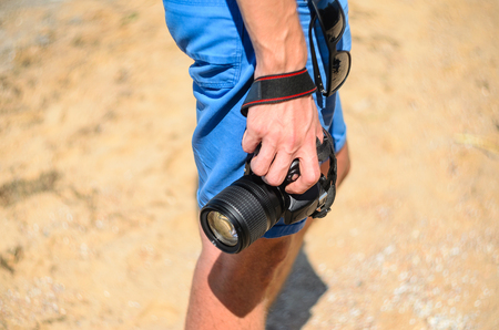 Dslr camera in the hands of a photographer on a sandy beach close upの写真素材
