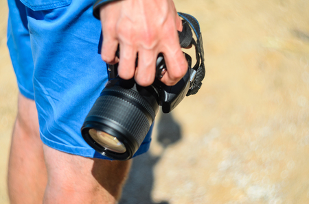 Dslr camera in the hands of a photographer on a sandy beach close upの写真素材