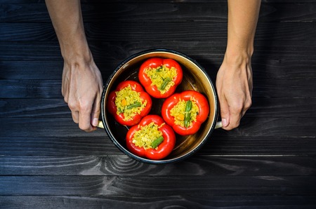 Chef holding a pan with four red stuffed peppers on dark rustic kitchen table background, top view. Cooking processの写真素材
