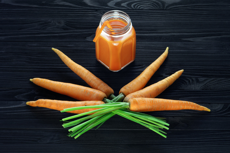 Fresh carrot juice in a glass jar with handle on a black wooden table and a bunch of fresh carrots top viewの写真素材