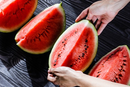 Man's hands take a slice of watermelon on black wooden table. Top view.の写真素材