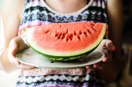 Girl in a colorful summer shirt holding a plate with a large slice of watermelonの写真素材