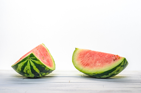 Two pieces of a watermelon on white wooden table on white background background front view. Blank minimalistic backgroundの写真素材