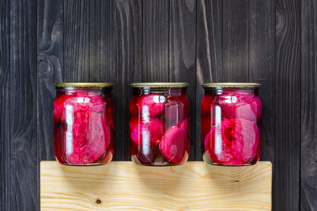 Canned homemade beetroot in three clear glass jars with wooden cutting board on a black wooden background top viewの写真素材