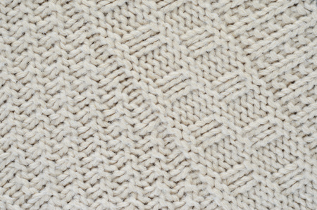 Texture of a beige knitted sweater close-up. Diagonally oriented pigtails on knitted fabric