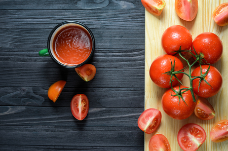 Tomato Juice in Green Enamel Mug on a Black Wooden Table with Fresh Branch of Tomatoes on a Wooden Cutting Board Top Viewの写真素材