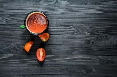 Tomato Juice in Green Enamel Mug on a Black Wooden Table Among Fresh Tomatoes Top View. Background with a Blank Space for Textの写真素材