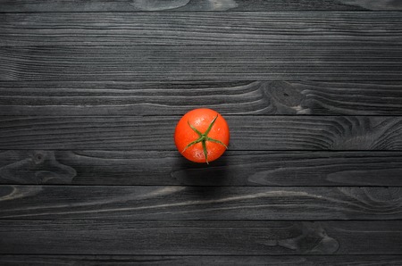 One Tomato in Center of Black Wood Background Top Viewの写真素材