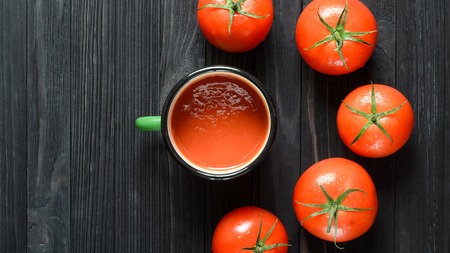 Tomato Juice in Green Enamel Mug on a Black Wooden Table Among Fresh Tomatoes Top View. Background with a Blank Space for Textの写真素材