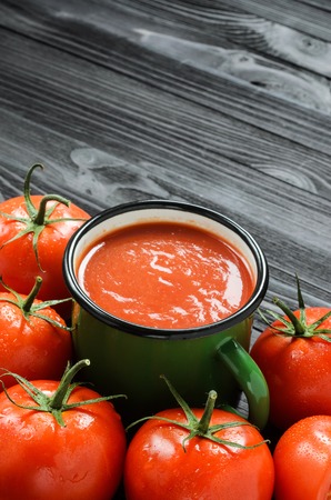 Tomato Juice in Green Enamel Mug on a Black Wooden Table Among Fresh Tomatoes Top View. Background with a Blank Space for Textの写真素材