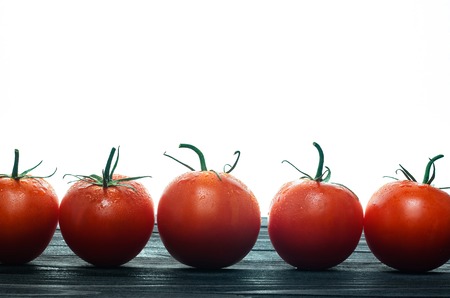 Red Tomatoes Standing in a Row on a Black Wooden Table Against White Background Close-Upの写真素材