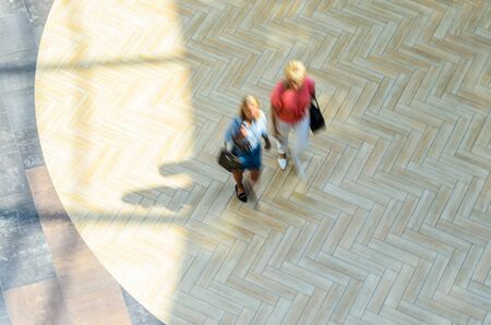Silhouettes of Two Walking People in the Atrium of a Large Public Building, View from Above. Blur in Motion, Long Exposure. Abstract Backgroundの写真素材