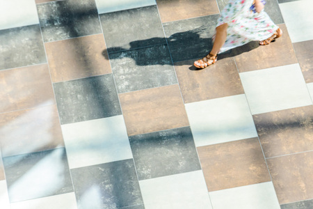 Silhouette of a walking woman with long shadow from above. Abstract background of blur in motion figure of a young woman in a public building hall top view. Blurred Abstract Background.の写真素材