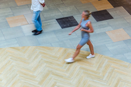 Silhouette of a walking woman, view from above. Abstract background of blur in motion figure of a young woman in a public building hall top view. Blurred Abstract Background.の写真素材
