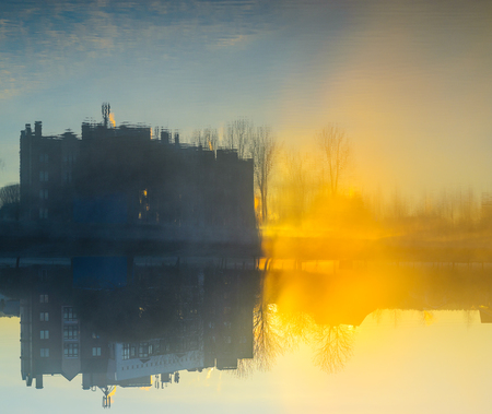 Weather conditions: a strong morning fog on a pond near residential buildings. Reflection of the facades of residential buildings at the surface of the water at dawn. Abstract weather backgroundの写真素材