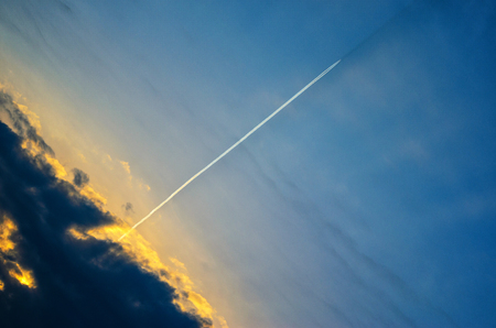 Bright white trail aircraft in the cloudy sky at sunset. Plane flies out of a thundercloud at sunsetの写真素材