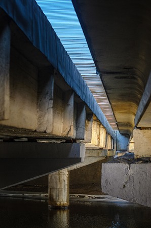 Type of concrete road bridge across the river view from below. Abstract industrial background with structural elements of an engineering structureの写真素材