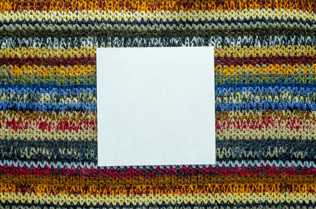 Colorful Knit Fabric Texture with White Card of Paper as Blank Space. Macro View of a Knitted Sweater. Blank Backdrop Mock-Upの写真素材