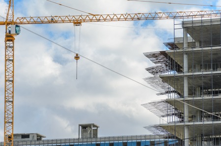 Construction site with crane and with unfinished skeleton of a high-rise building made of reinforced concrete against cloudy skyの写真素材