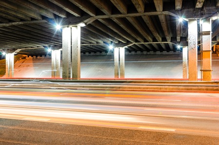 Bottom View on Concrete Road Bridge Structures. Night Traffic with Light Trails on Highway Interchangeの写真素材
